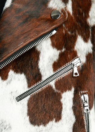 Close-up of a brown and white cowhide leather jacket with zippers.