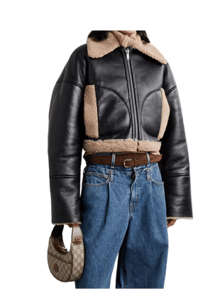 Person wearing a black leather jacket with shearling collar and blue jeans, holding a handbag.
