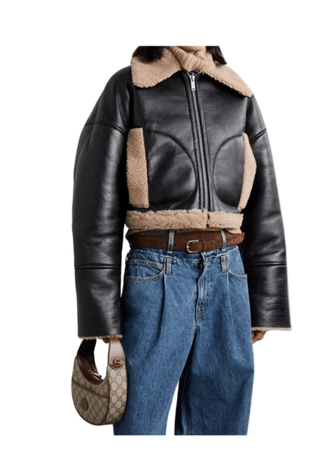 Person wearing a black leather jacket with shearling collar and blue jeans, holding a handbag.