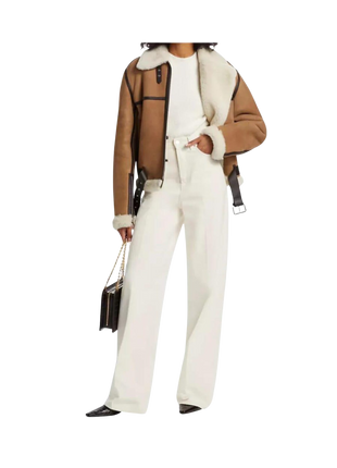 Person wearing a brown jacket with sheer panels, white top, and white pants 